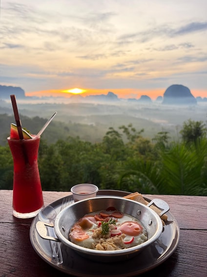 A meal with a drink and a scenic view of a sunset over a mountainous landscape. 4