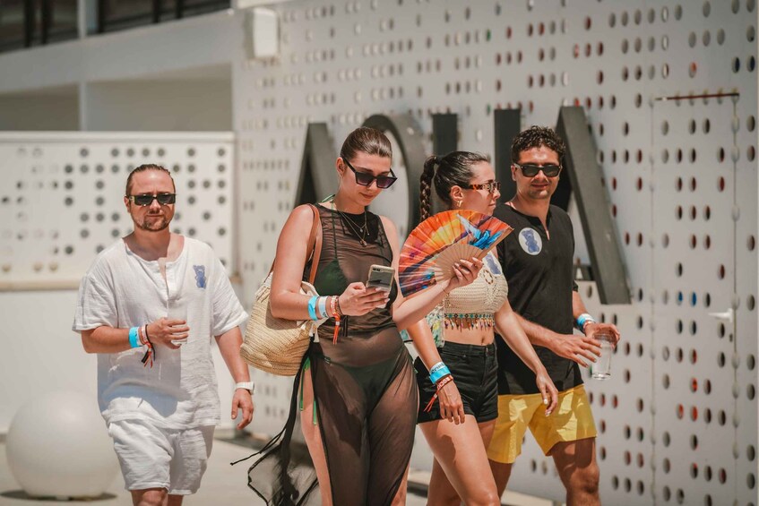A group of people walking outdoors, some holding drinks and one holding a fan. 2