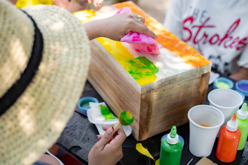 A person painting a wooden box with colorful paints. 1