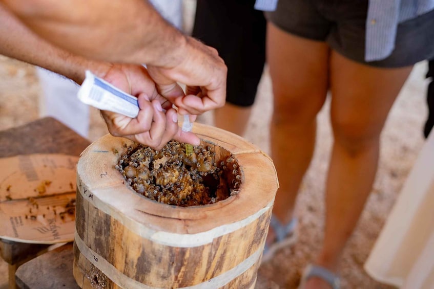 A person using a tube to fill a wooden barrel with a granular substance. 2