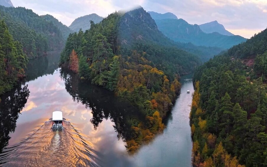 A boat on a calm river surrounded by forested mountains. 1