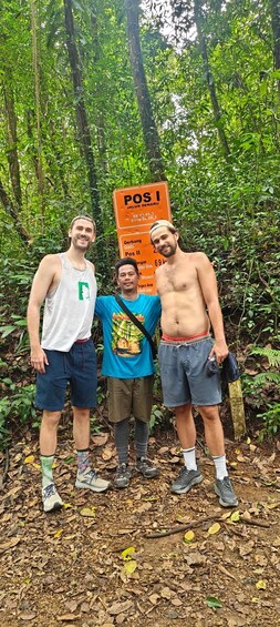 Three people standing in a forest with a signpost in the background. 2