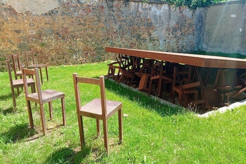 Outdoor wooden chairs and a metal table on a grassy area with a stone wall in the background. 2