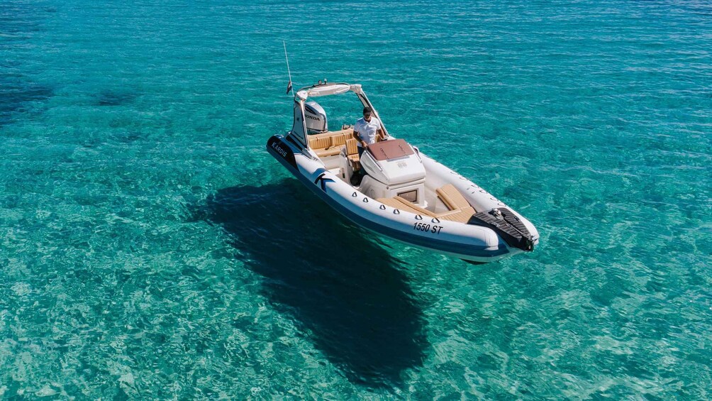 A white motorboat with a canopy and a person on board, floating on clear turquoise water. 3