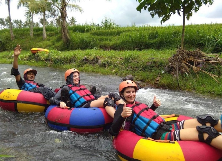 Three people rafting down a river surrounded by greenery. 1