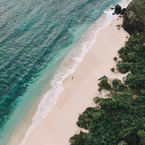 A beach with clear turquoise water, a person walking along the shore, and dense greenery on the right. 2