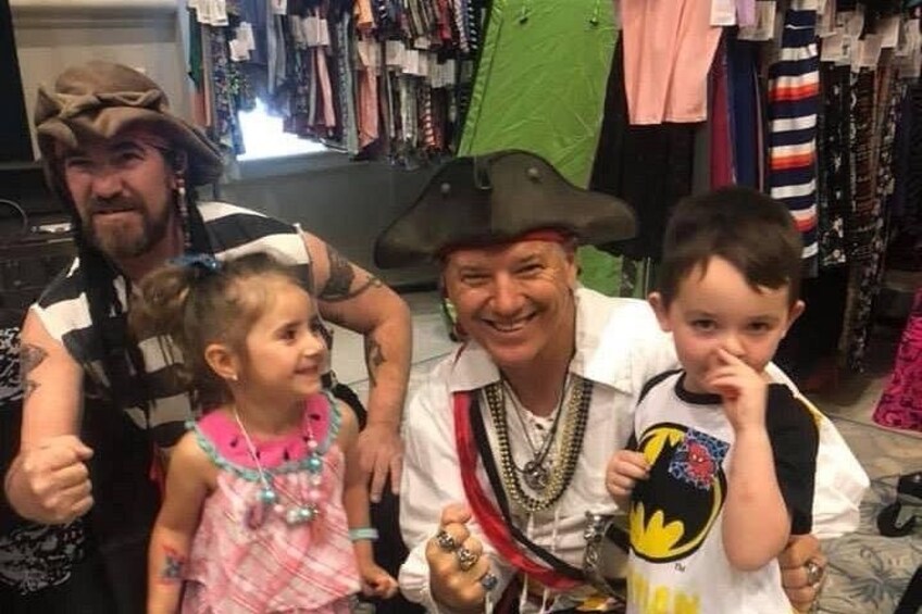 A man in pirate attire with two children, one in a pink dress and the other in a black and white shirt, in a clothing store. 5