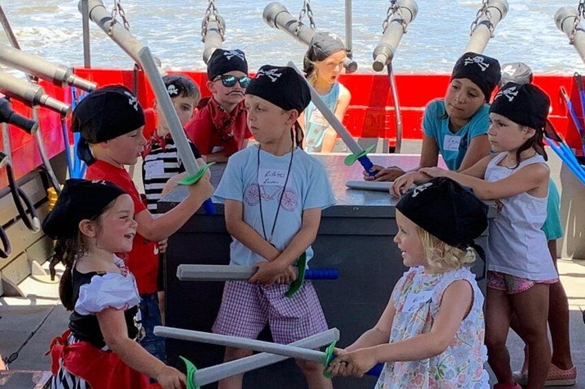 Children on a boat with cannons, wearing pirate hats and holding swords. 3