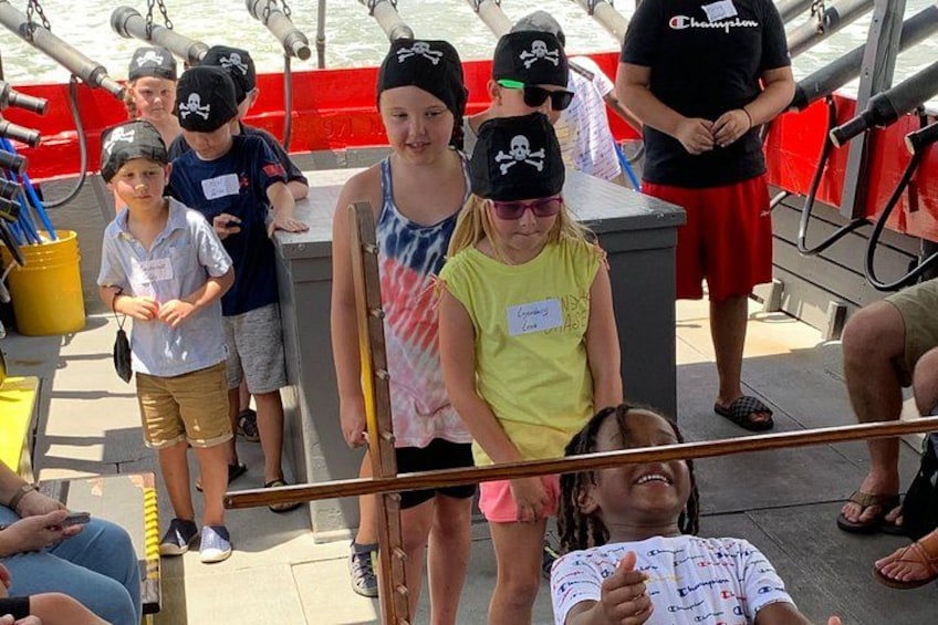 People on a boat wearing pirate hats and holding a wooden plank. 1