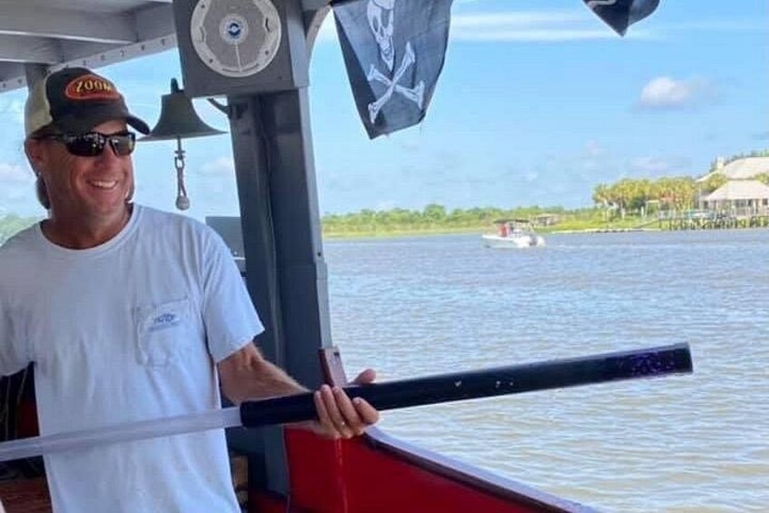 A person holding a boat's steering wheel, a flag, and a boat's cabin. 4