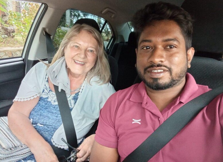 Two people seated in a car with a window view of greenery outside. 1