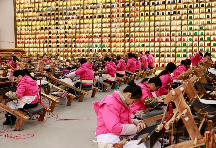 A group of people in pink jackets working on wooden horse-shaped structures in a workshop with a colorful wall in the background. 5