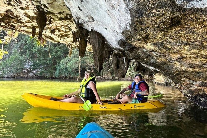Two people kayaking in a yellow kayak on a river with a cave in the background. 3