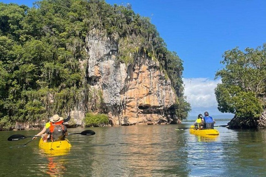 Two people kayaking on a calm river surrounded by cliffs and dense vegetation. 2