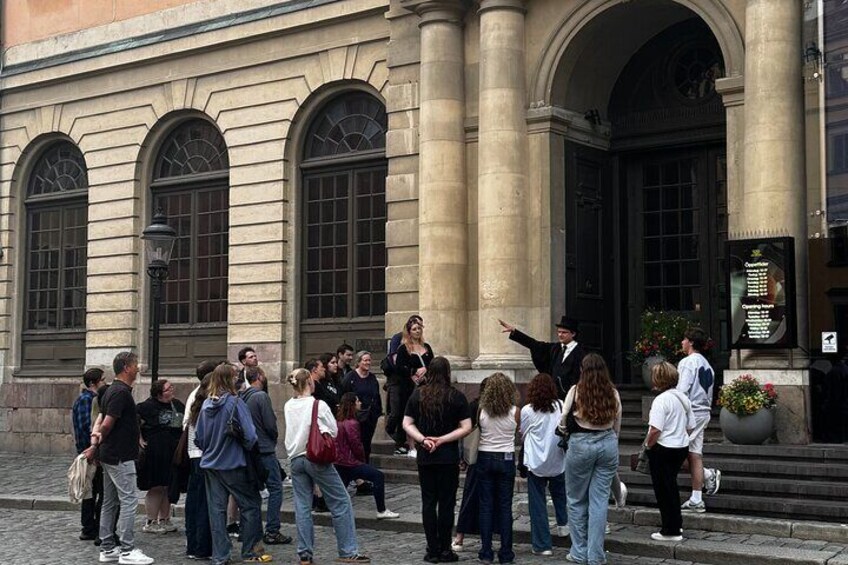 A group of people gathered outside a building with arched windows and a large door. 3