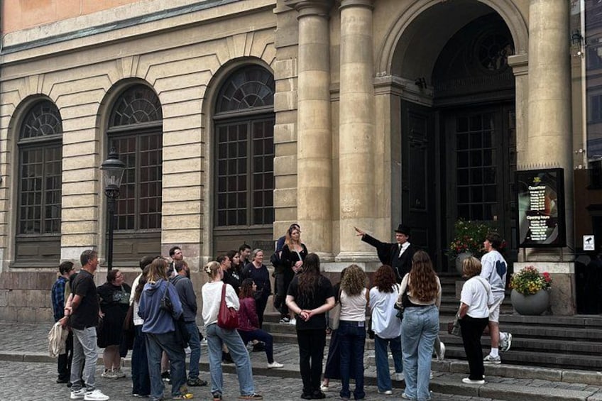 Un grupo de personas frente a un edificio con ventanas arqueadas y una puerta negra. 2