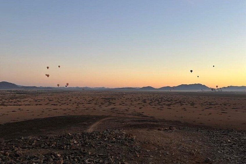A desert landscape with a dirt road and several hot air balloons in the distance. 3