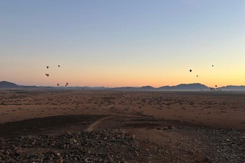A desert landscape with scattered hot air balloons and a dirt path. 3