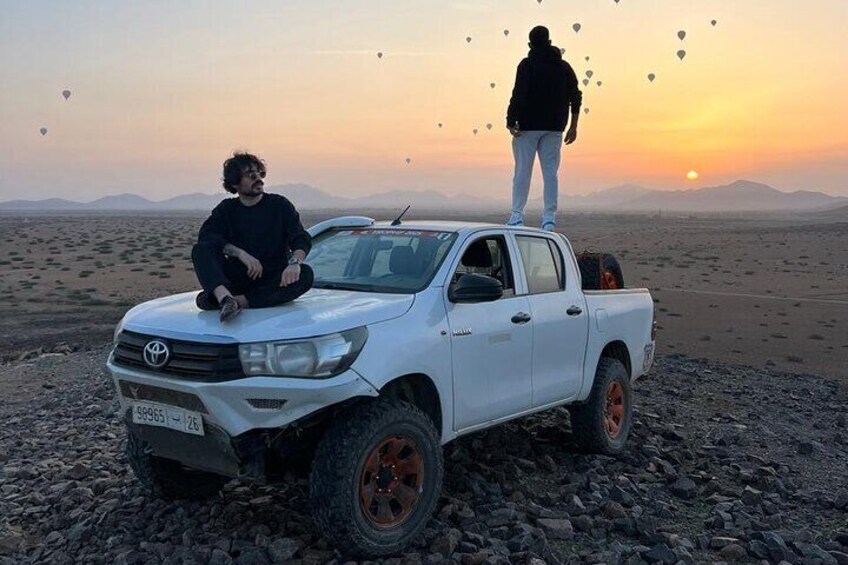A white pickup truck with a person sitting on the hood and another standing in the bed. 4