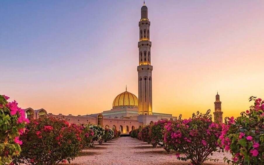 A mosque with a tall minaret and a dome, surrounded by a garden with pink flowers. 3