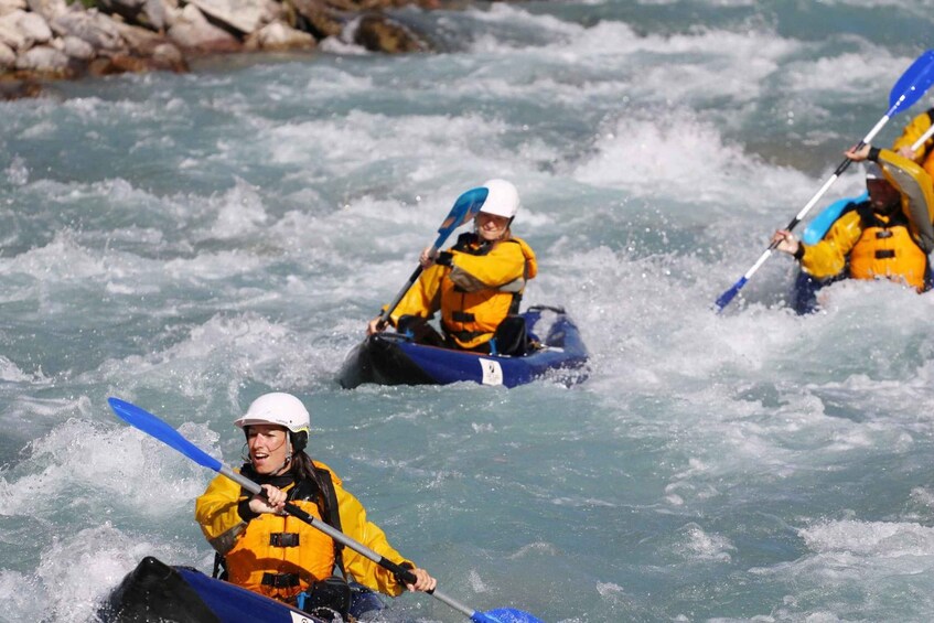 Three kayakers in yellow helmets and jackets navigating a river with white water rapids. 3