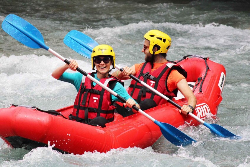 Two people in a red inflatable raft on a river, wearing helmets and life jackets. 4