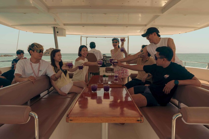 A group of people on a boat, seated around a table with drinks. 3