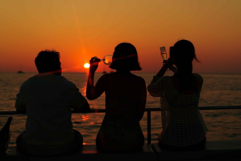 Three people sitting by a railing during sunset, overlooking the ocean. 4