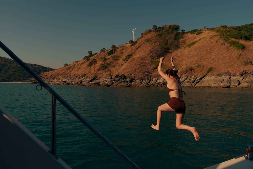 A person jumping into water from a boat with a hilly landscape and wind turbines in the background. 5