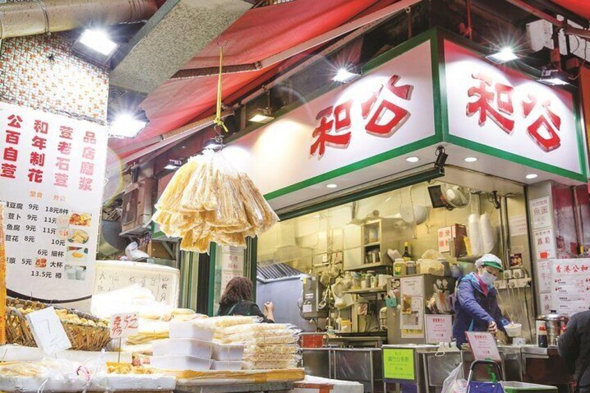 A street food stall with a sign in a foreign language, food items displayed outside, and a person working inside. 4