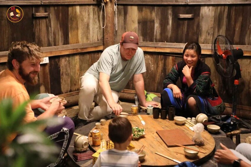 A group of people seated around a wooden table in a rustic setting, with various dishes and utensils. 5