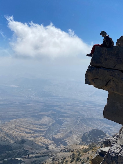 A person sitting on a rock ledge overlooking a valley. 1