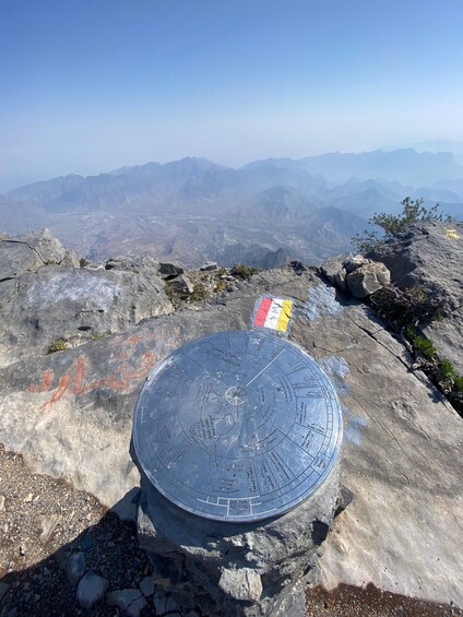 A circular stone with inscriptions and a compass rose, surrounded by rocky terrain and distant mountains. 5