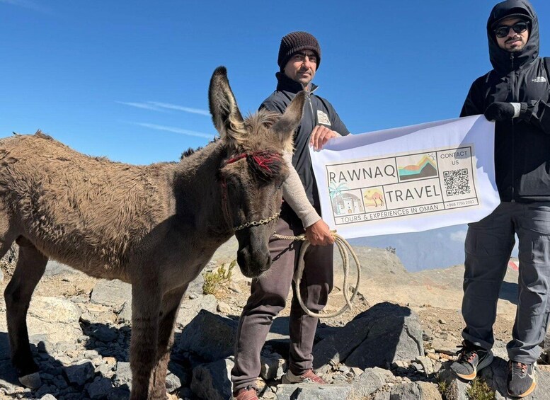 A donkey on rocky terrain with two people holding a travel brochure. 3