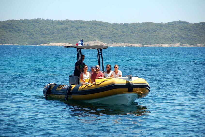 A yellow inflatable boat with passengers on a calm sea, surrounded by clear blue water and a distant green shoreline. 5