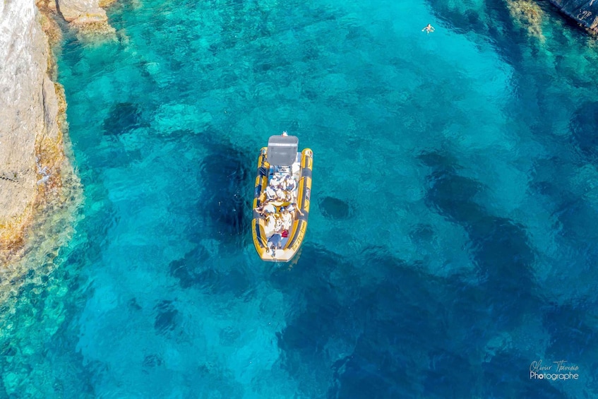 An aerial view of a small boat with people on a clear blue sea, surrounded by rocky coastline. 4