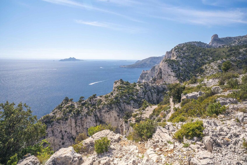 A coastal landscape with rocky cliffs, a clear blue sea, and distant islands. 3
