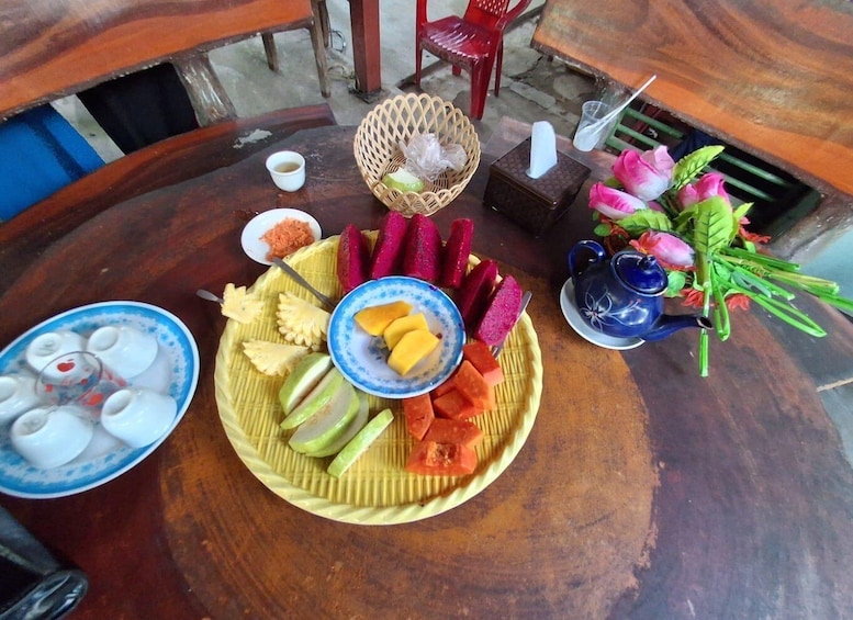 A round wooden table with a fruit platter, a blue teapot, and a small bowl of sugar. 3
