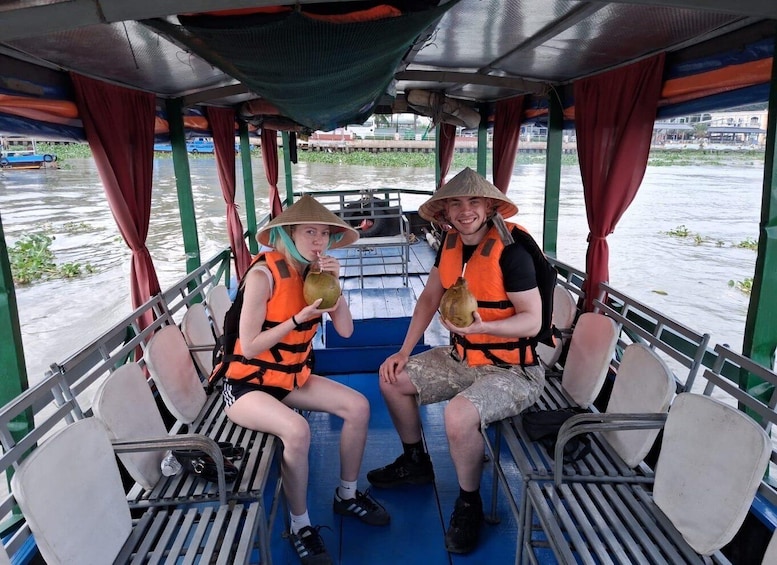 Two people on a boat, wearing life jackets and hats, with water and greenery visible through the windows. 5