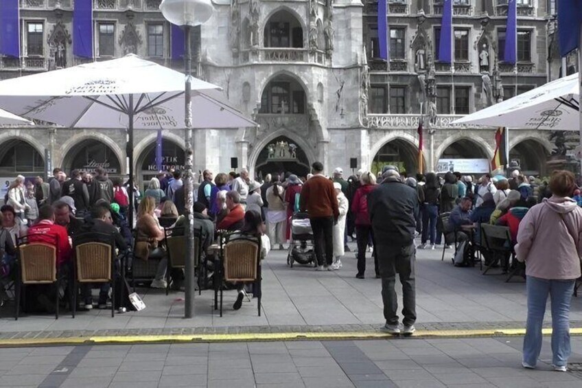 A crowded outdoor café with people seated at tables, surrounded by historic architecture. 2