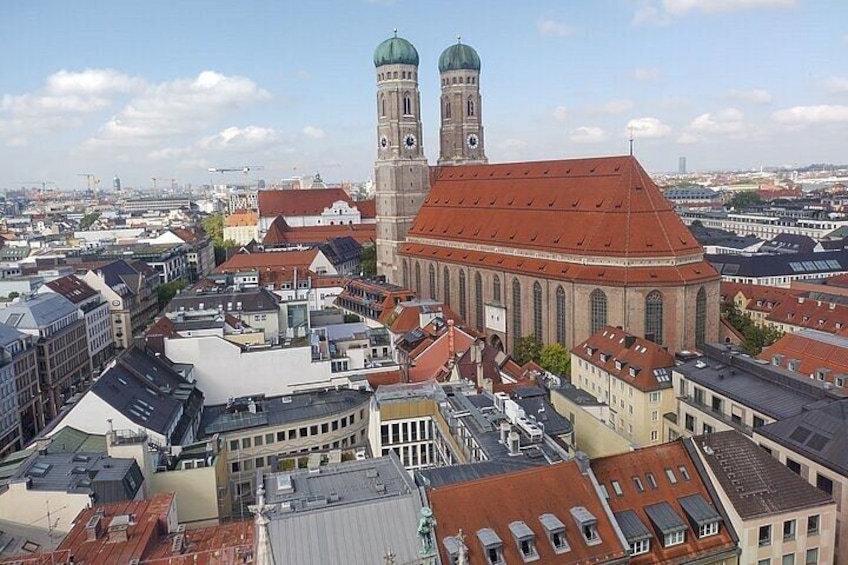 A cityscape with a prominent church featuring two towers, surrounded by densely packed buildings with red roofs. 1