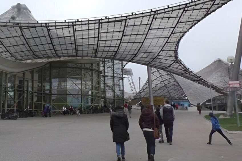 A modern architectural structure with a curved glass facade and a distinctive metal roof. 3
