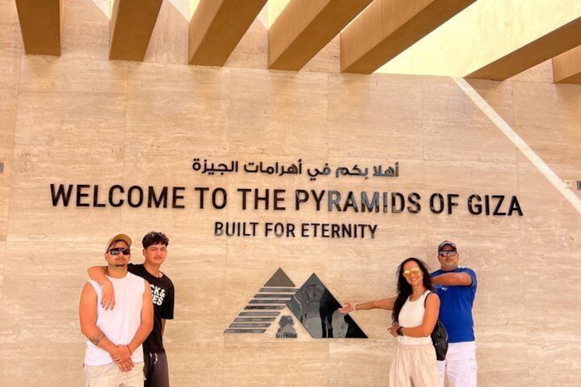 A group of people standing in front of a sign that reads 'WELCOME TO THE PYRAMIDS OF GIZA BUILT FOR ETERNITY.' 5