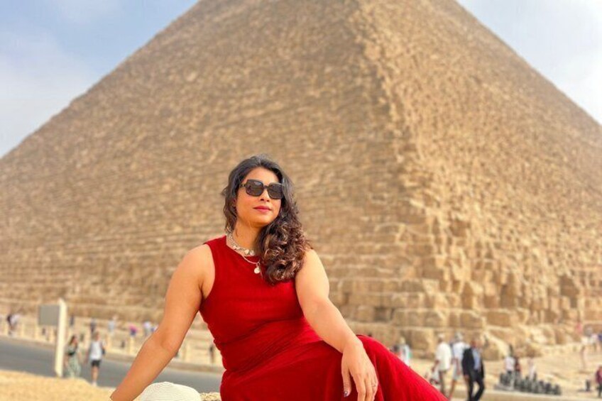 A person in a red dress sitting in front of the Great Pyramid of Giza. 1