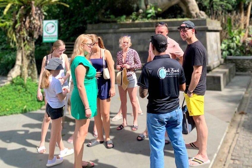 A group of people standing on a sidewalk, a sign with a prohibition symbol, and a tree in the background. 2