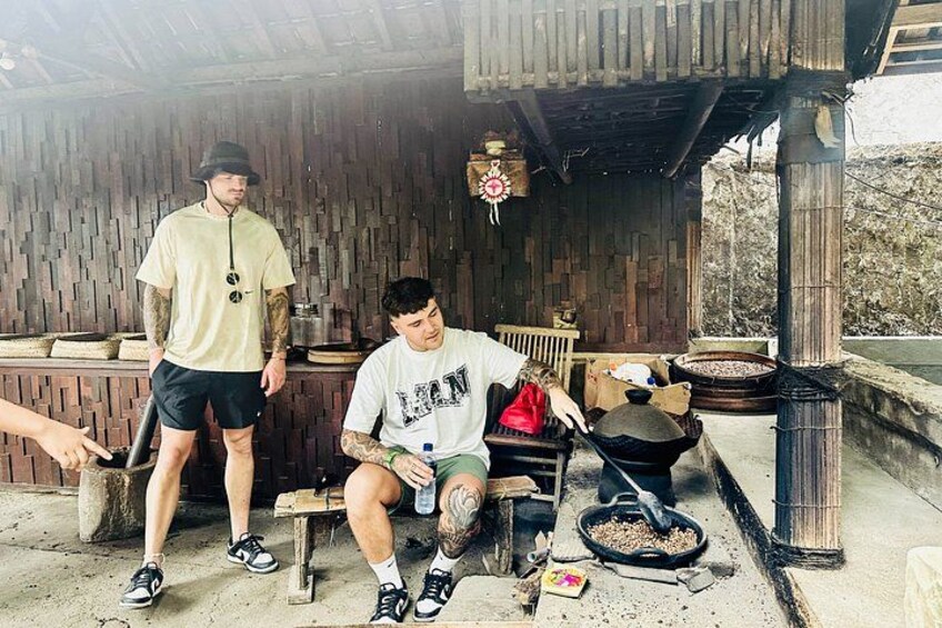 A rustic outdoor setting with wooden structures, a person sitting on a bench, and another standing nearby. 4