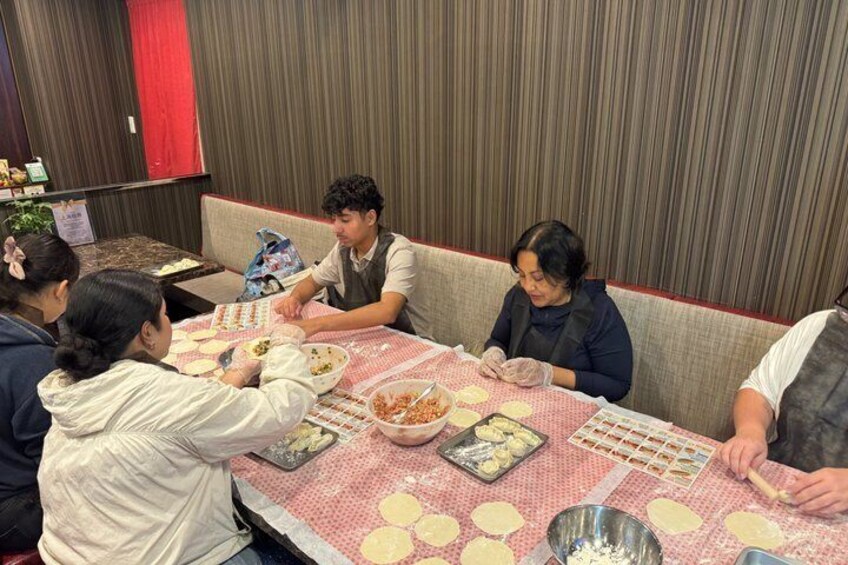 A group of people making dumplings at a table with a red tablecloth. 3