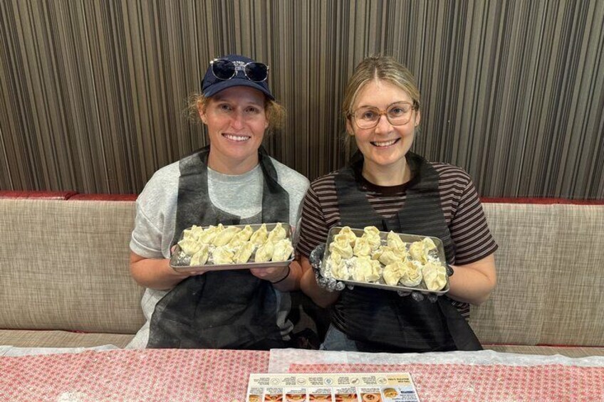 Two people holding trays of food at a table with a floral tablecloth. 1