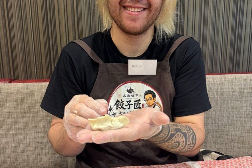 A person wearing a black apron with a name tag and a logo, holding a dumpling. 2