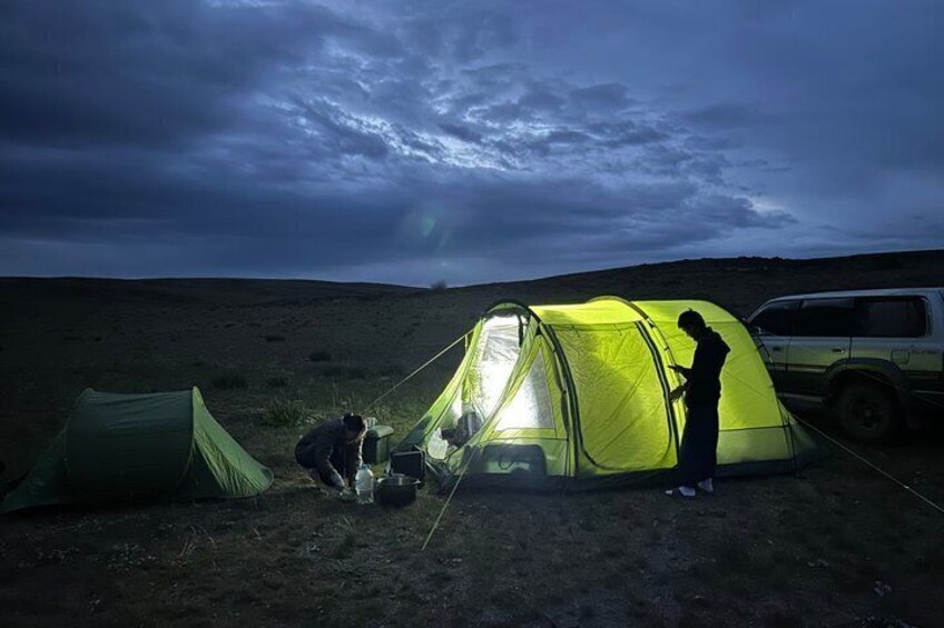 A person setting up a tent in a grassy field with a vehicle nearby. 1